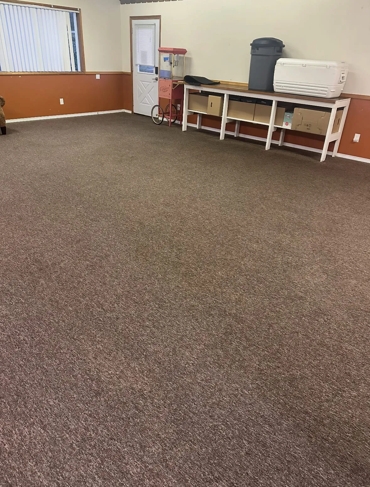 A large clubhouse room in Oak Harbor with evenly clean brown carpet after cleaning, a popcorn cart and shelving along the back wall