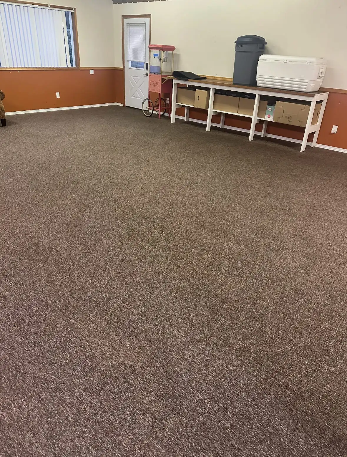 A large clubhouse room in Oak Harbor with evenly clean brown carpet after cleaning, a popcorn cart and shelving along the back wall