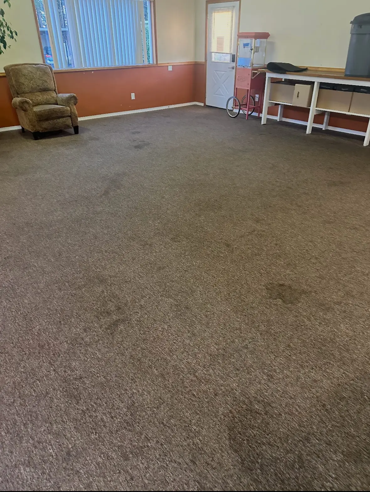 A large Oak Harbor clubhouse room before cleaning, with dark spots and stains scattered across the brown carpet from the door to the middle of the room
