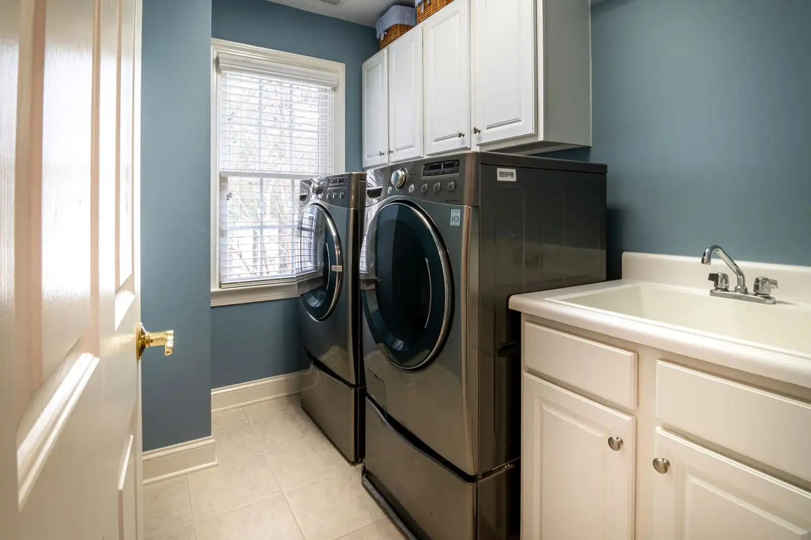 A laundry room with a front-load washer and dryer side by side beside a utility sink and white cabinets