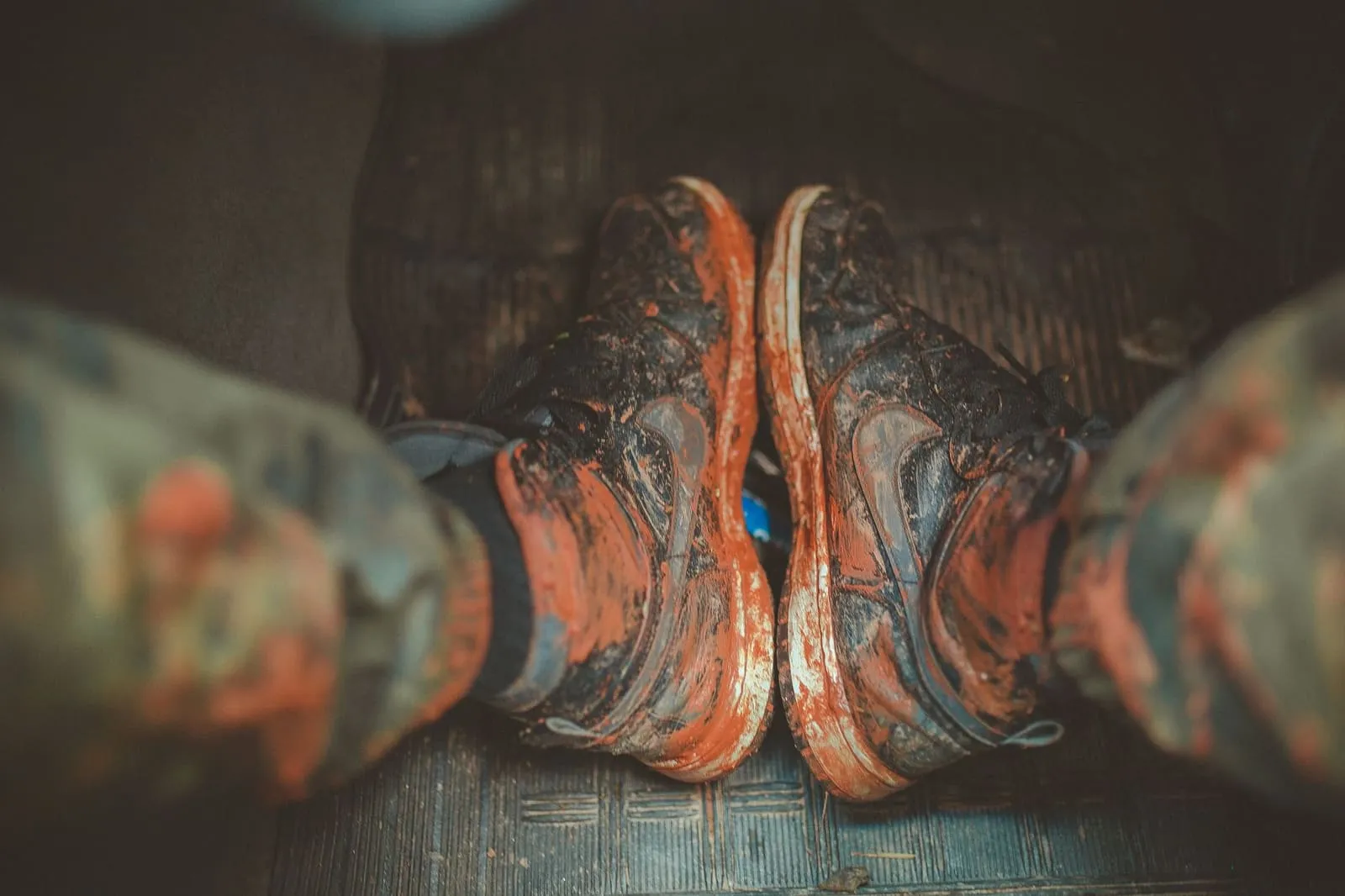 A pair of muddy sneakers caked in orange-red mud, the kind of dirt that gets tracked onto carpet