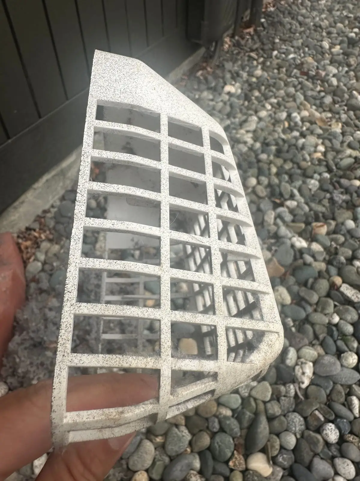 The same white dryer vent guard after cleaning, its grid clear so the stones below show through